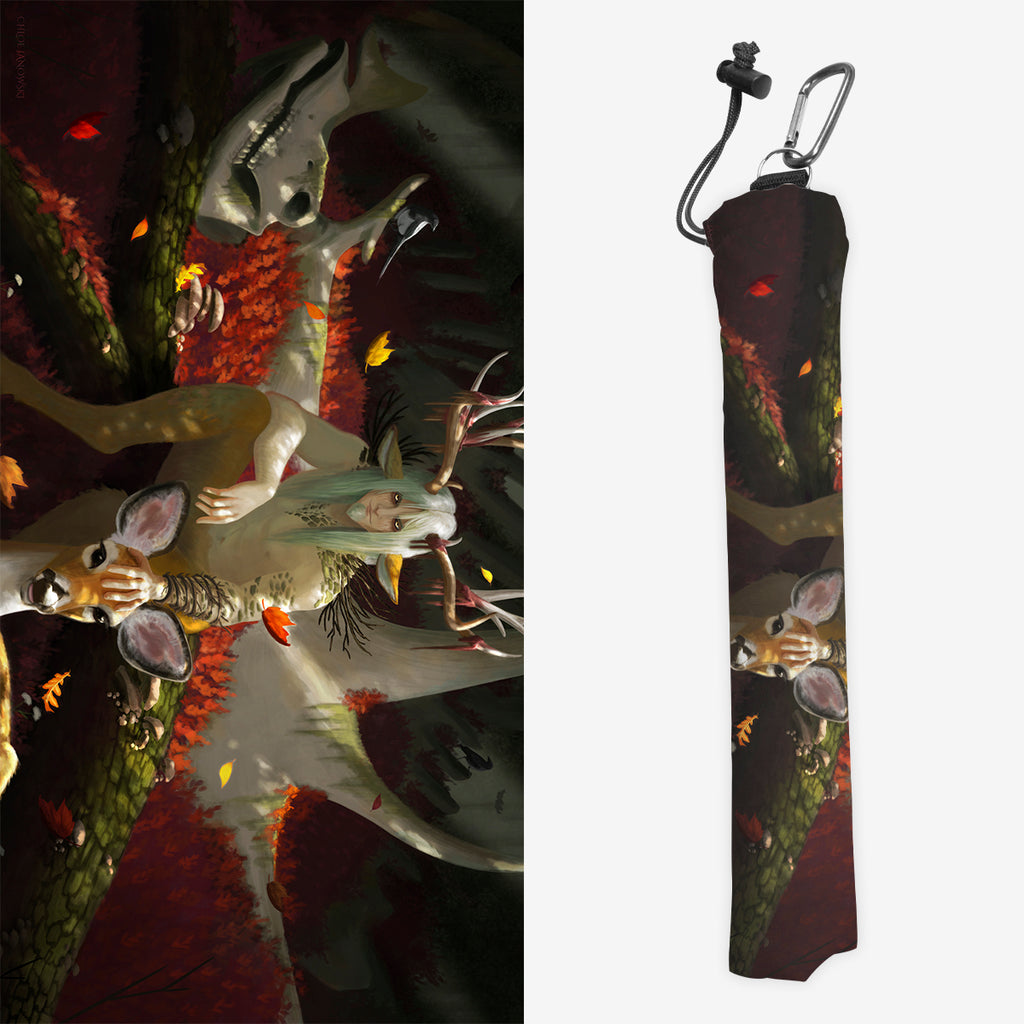 Playmat bag of Berstuk, The Forest God by Chloe Janowski. It shows a person with large antlers sitting on a tree stump. There is a deer to the right of this person and a deer skull to the left. Leaves are falling for nearby trees.