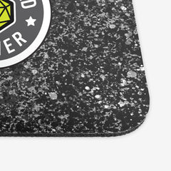 A close-up of a classic mousepad with grey, white, and black splattered paint behind a circular logo. The logo is white and grey with a green 20 sided dice in the middle. The white text around the dice reads “Vaccinated Gamer.”