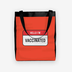 A red day tote with a red and white label at the center. The red part of the label reads “Hello I’m” in white text. The white part of the label reads “Vaccinated” in black text.