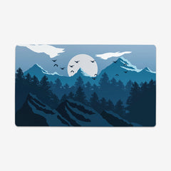 Blue Winter Forest playmat by Carbon Beaver. Landscape of trees and mountains. The sun is setting and birds are flying in the sky. All of the colors are shades of blue.Winter Forest Thin Desk Mat - Carbon Beaver - Mockup