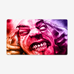 Playmat of Infected Mind by Why Try Designs. A orange, red, pink, and purple drawing of a man with his hands on his head. He is making a face as if he's in pane. His eyes are all white, he has scars on his face, and all his teeth are showing.